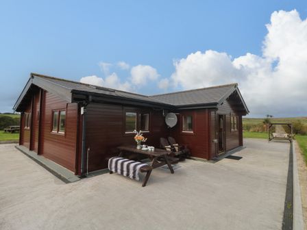 A wooden house with a picnic table and chairs outside on a concrete patio at Chywolow Lodge in Penzance