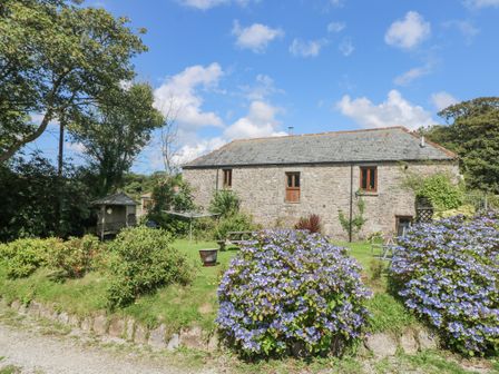 A stone cottage with a slate roof surrounded by garden shrubs and flowers at Mill Nancegollan nr Porthleven