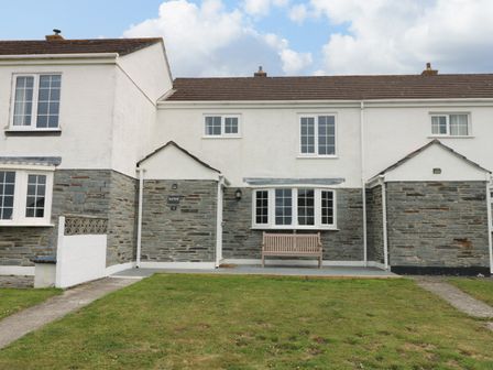 A row of houses with stone lower walls and white upper walls with a bench outside at Bayview in Watergate Bay