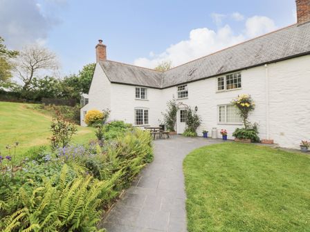 An exterior of a white stone house with a chimney a garden with plants flowers and grass at Withan Farm Wing in Helford