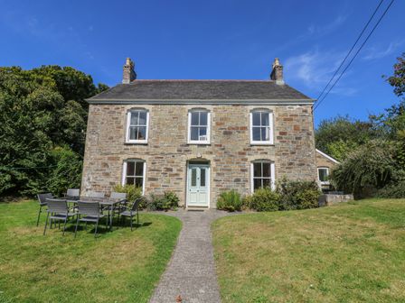 A stone house with four windows and a door with outdoor table and chairs on grass at Goshen Farm in St Agnes