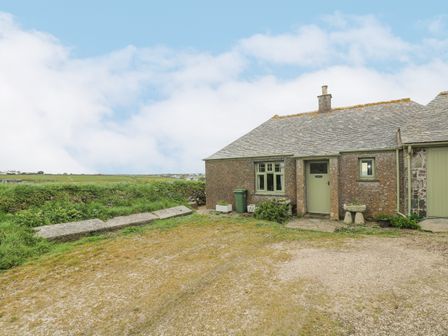 An exterior view of a stone cottage with green door and windows and a gravel driveway at Parc An Castle Cottage in Lizard