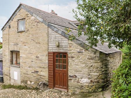 A stone house with a wooden door and windows surrounded by trees and plants at Apple Loft in Lostwithiel