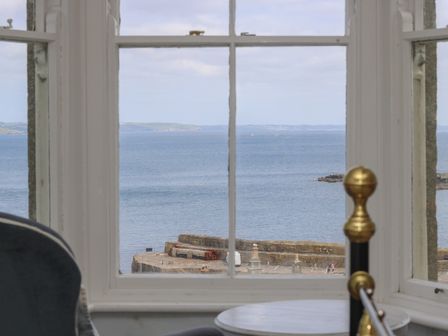 A window view overlooking the sea with a stone pier and distant hills at Lookout in Mousehole