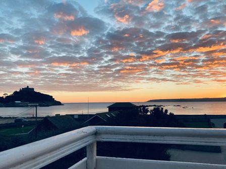 A coastal view at sunset with a castle on a hill to the left and buildings near the shore at Sea Breeze in Marazion