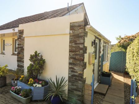 The exterior of a small house with stone and cream walls a tiled roof potted plants and a blue wooden gate at Respryn Mevagissey