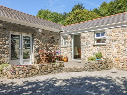 An outdoor stone patio with a wooden table and chairs next to a stone building at Pond Cottage in Stithians