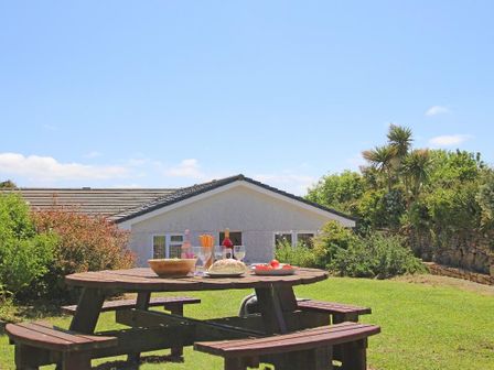 A wooden picnic table with food and drinks in a garden with a house and plants at Carne Vue in Penzance