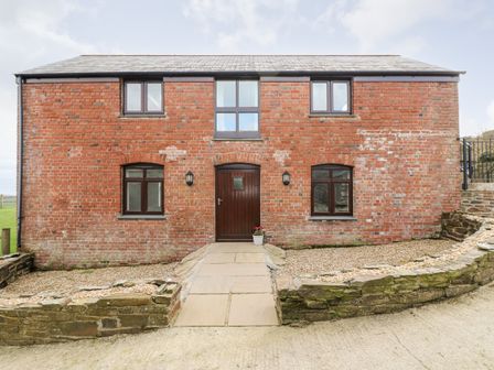 A red brick house with a central wooden door and four windows at Castle Dore Barn in Fowey