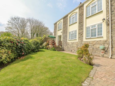 A garden with grass bushes and a stone house with windows at Secret Garden in St Agnes