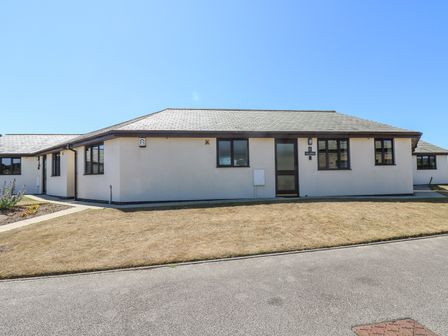 A single-story building with white walls and multiple windows on a street with dry grass at Sea Shore in Marazion