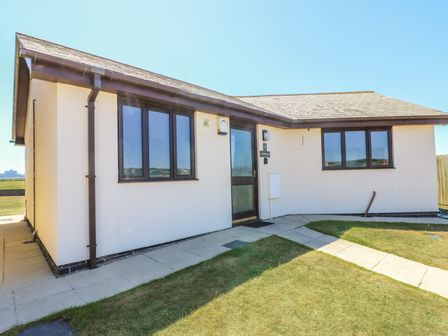 A single-story house with white walls and brown window frames and door at Shoreline in Marazion