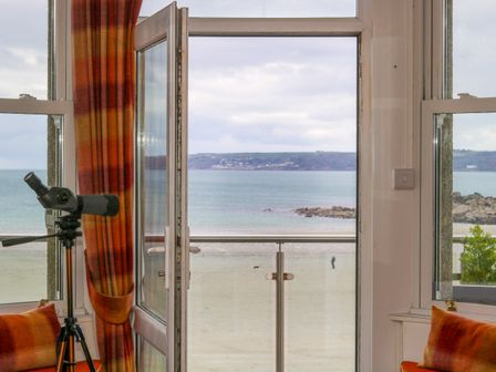 A room with orange curtains and cushions a telescope by an open glass door overlooking a beach and sea at Mount View in Marazion