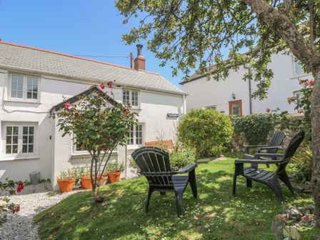 A garden with black chairs and potted plants outside white cottages at Elfin Cottage in Porthleven