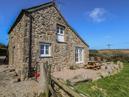 A stone cottage with white framed windows and doors with outdoor wooden table and chairs on gravel at Boar's House in Penzance