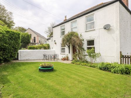 A garden with green grass and a table with four chairs outside a white house at Angarrack Farmhouse in Hayle