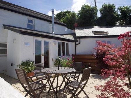 A patio area with a round wooden table and four chairs outside a white house at Godrevy Cottage in Hayle