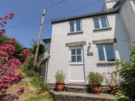 Exterior of a white two-story house with a white door and four windows surrounded by pink flowers and greenery at Little Hamlin in Rilla Mill Nr Callington
