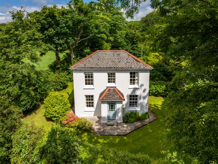 A white two-story house with a gray roof surrounded by trees and greenery at Penwarne Lodge in Mawnan Smith