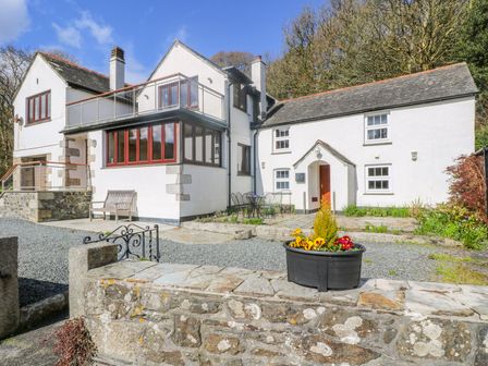 The exterior of a white building with multiple windows a bench a table with chairs and a flowerpot on a stone wall at Carne Mill in Manaccan