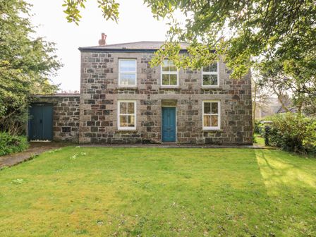 A stone house with four windows and a blue door surrounded by grass and trees at Banneth in Helford
