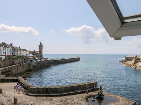 A harbor with people near a cannon and a stone wall extending into the sea at Sea Star in Porthleven