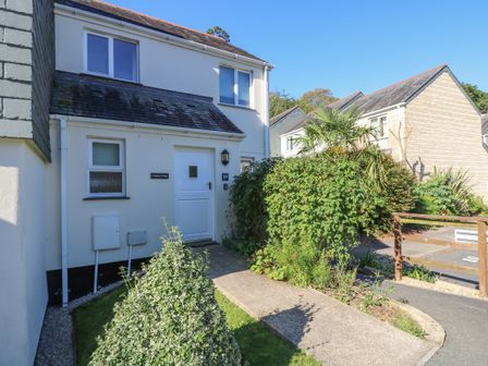 The exterior of a two-story house with a white door and windows surrounded by bushes and greenery at Hedgehog Cottage in Falmouth