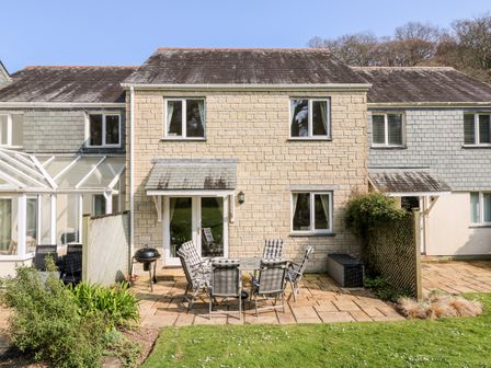 A stone house with a patio set and grill in the backyard at Sild Cottage in Falmouth