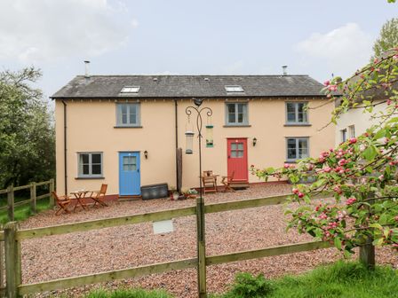 A beige two-door house with blue and red doors and small outdoor tables and chairs near the doors at Plum Cottage in Colebrooke near Crediton