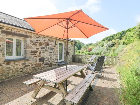 An outdoor patio with a wooden picnic table and umbrella next to a stone building at Roosters in Lostwithiel