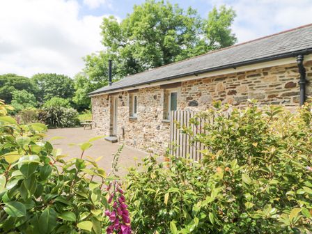 A stone exterior building with small windows and a wooden gate surrounded by green shrubs and trees at Wagon House in Lostwithiel