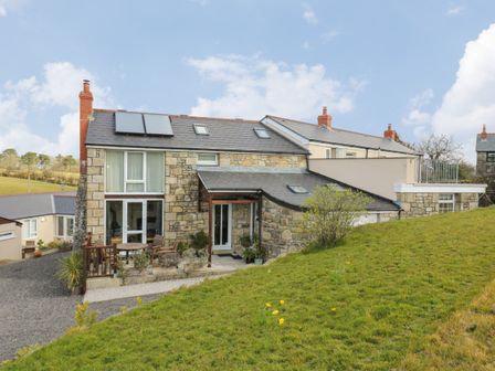 A stone house with a patio and outdoor furniture on a grassy slope at Mynheer Farm Barn Nr Portreath
