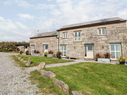 A stone house with solar panels on the roof surrounded by gravel driveway and grass at Black Rock in St Austell