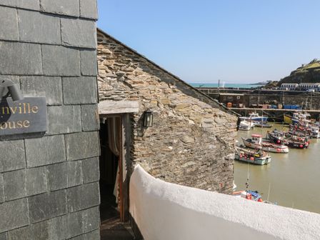 A view of a stone building with a balcony overlooking a harbor with boats at Glanville House in Mevagissey