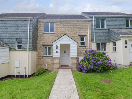 A stone-fronted house with a white door and a pathway leading to it with a flowering bush on the right at Flotsam in Falmouth