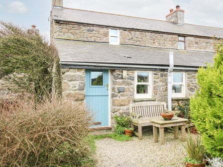 The exterior of a stone cottage with a blue door a wooden bench and table outside surrounded by plants and bushes at Gurnard's Cottage in St Ives