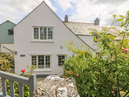 A white cottage with multiple windows a garden with green foliage and flowers and a stone wall at Parwin in Tintagel