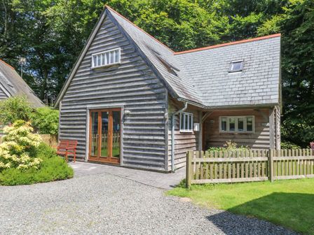 A wooden house with a slate roof and a small fenced garden near a gravel driveway at Oaklands Near Boscastle