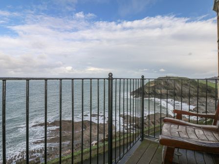 A balcony with wooden chairs and metal railing overlooking a rocky coastline and ocean at Seasiders in Ilfracombe