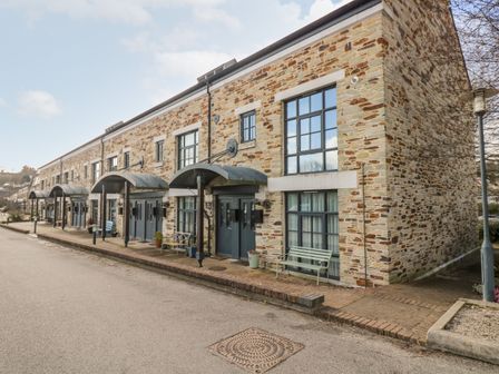 A row of stone townhouses with blue doors benches and metal canopies over entrances at Riverview in Lostwithiel