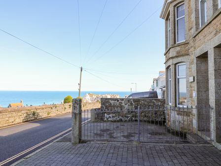 A paved driveway with a metal gate next to a stone building overlooking a road and the sea at Porthmeor Beach House in St Ives