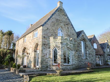 A stone house with arched windows and doors and a lawn at Lost Barn in Watergate Bay