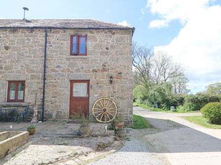 A stone house with a wooden door and windows with a large wooden wheel leaning against the wall at Courtyard in Nancegollan nr Porthleven