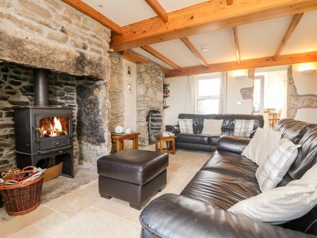 A living room with a wood burning stove two leather sofas an ottoman and stone walls at Boslow in St Just