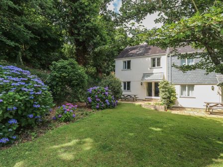 A garden with grass, bushes, and flowers in front of a two-story house at Bramble Cottage in Falmouth