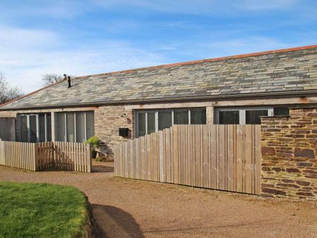A stone building with a tiled roof and wooden fencing in front at The Old Dairy in Padstow