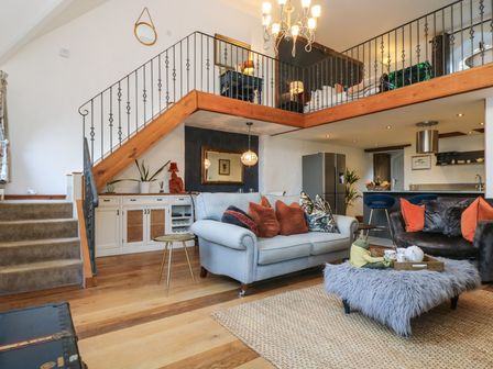 A living room with sofas cushions and a fluffy ottoman under a mezzanine at Hideaway in Watergate Bay