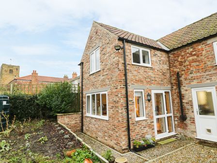 Exterior view of a two-story brick house with white framed windows and doors surrounded by a garden at Sunnyside Garden Cottage in Husthwaite