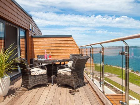 An outdoor wooden deck with a round table and four wicker chairs overlooking a body of water at Bayview in Brixham