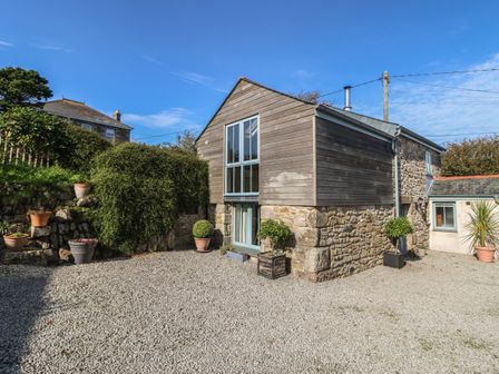 An exterior view of a stone and wood building with potted plants and a gravel ground at Hay Loft in Bolenowe Nr Portreath